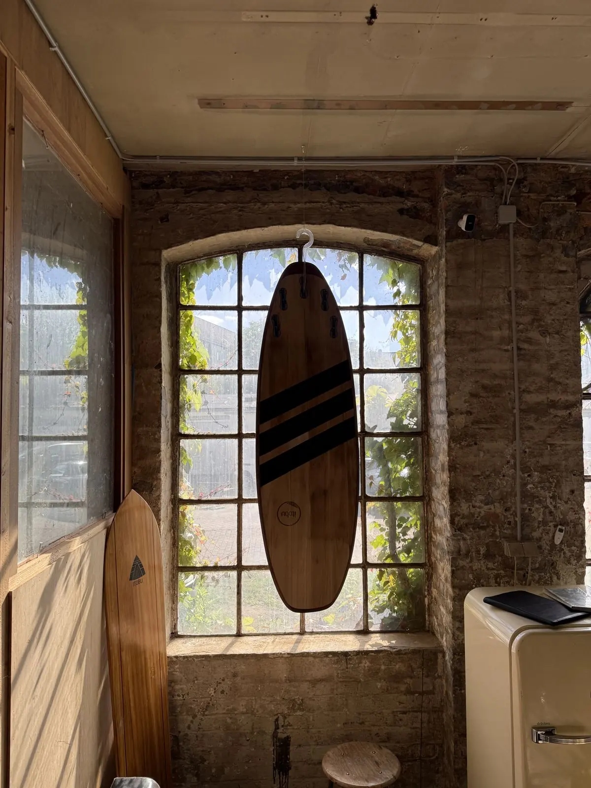 Holzsurfbrett hängt vor einem sonnigen Sprossenfenster im Ausstellungsraum