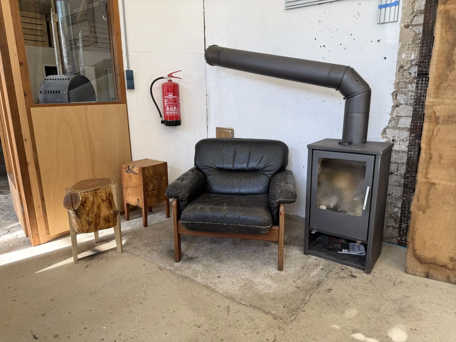 Alter Ledersessel mit Holzhockern neben einem Kaminofen in der Werkstatt